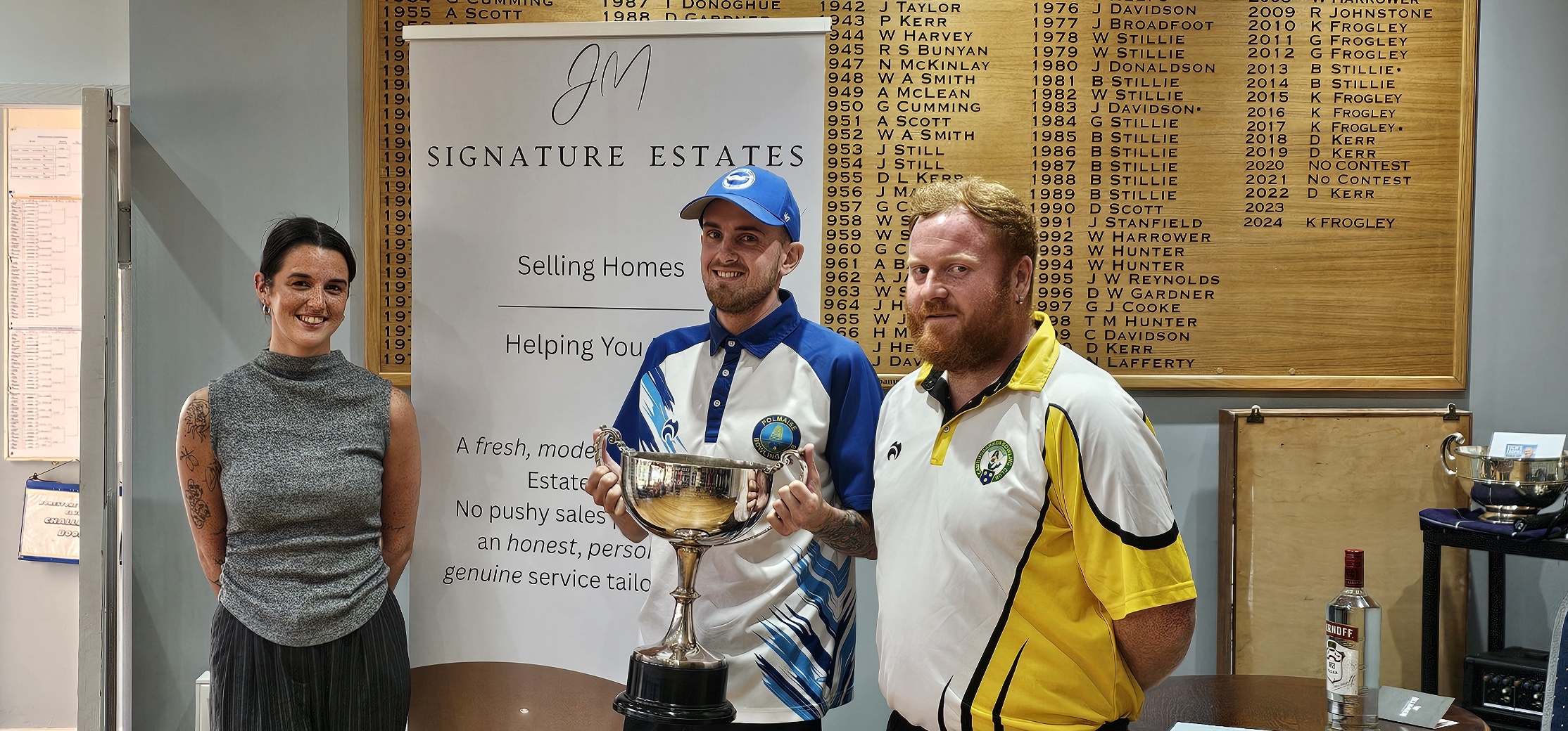 Aaron Furzer receives the Stirling Area and District Champion of Champions trophy following his 21–19 victory over James Wray, alongside the event sponsor and his opponent.